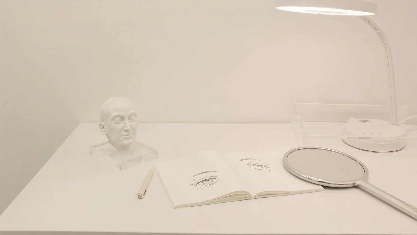 Eyelid planning sketches, a hand mirror and task light on a clean consultation table.