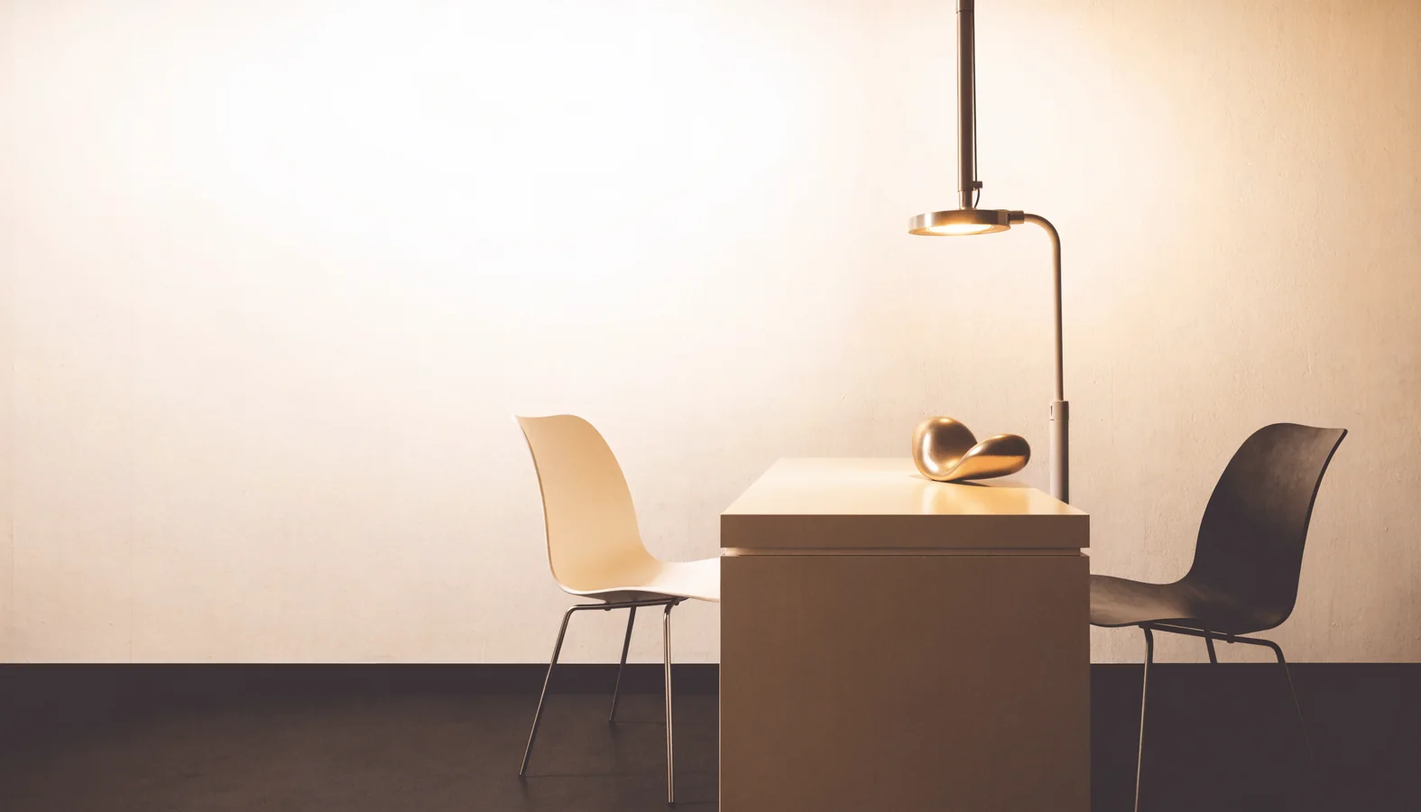 Minimalist private consultation room with two chairs, a clean desk and focused examination light.